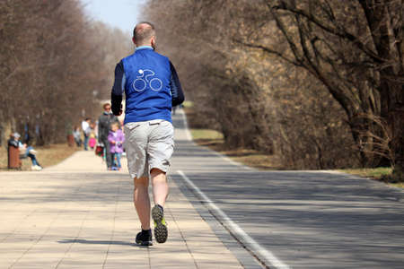 Man in shorts running on sidewalk along the park street, rear view. Runner in city, workout in...