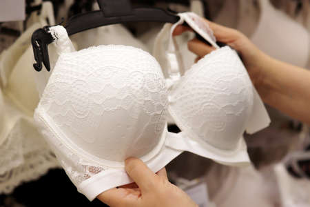 Woman chooses white lace bra in lingerie store. Concept of female fashion, different sizes of wedding underwearの写真素材