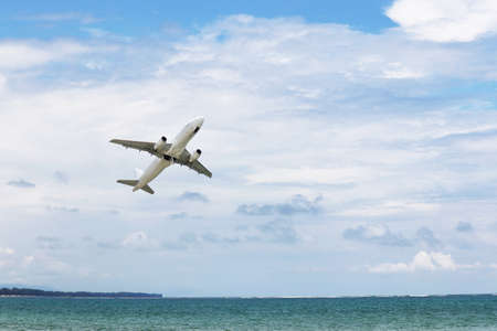 Airplane flies over the sea and coast on white clouds background. Commercial plane taking off and...
