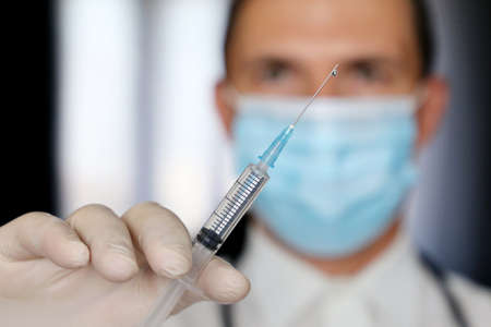 Doctor with syringe in hand, man in medical mask and latex gloves preparing to injection. Concept of vaccination during  pandemicの写真素材