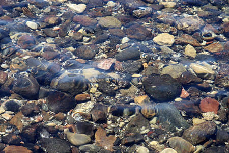 Transparent water with a pebble bottom, stone beach. Soft sea waves on clear water surface