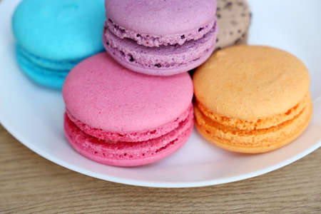 Macaroons in a white plate close up, colorful sweets. Strawberry, blueberry, vanilla and orange...