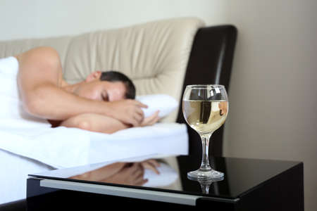 Man sleeping in bed, glass of white wine in foreground. Concept of home relax, alcohol abuseの写真素材