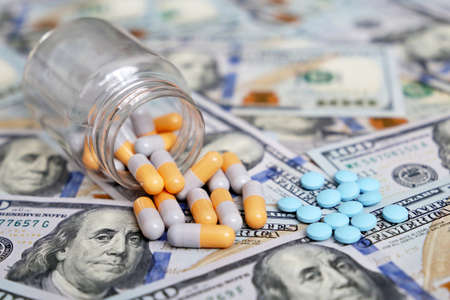 Pills and capsules on US dollar bills, medication scattered from the bottle. Concept of health care,...