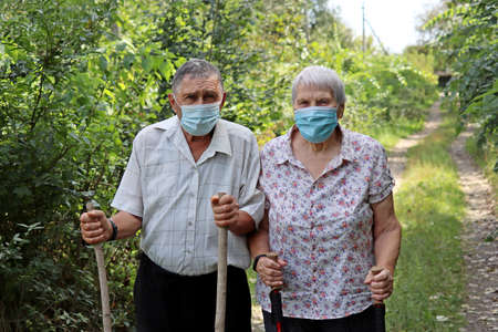 Elderly couple in protective face masks walking with canes on nature background. Safety during...