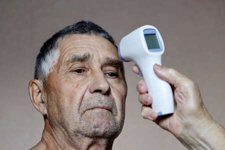 Measuring body temperature of elderly man. Digital infrared non-contact thermometer in hand, concept...