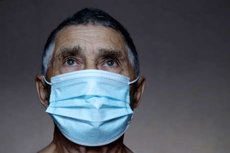 Portrait of elderly man in medical mask looking up on dark background.の写真素材