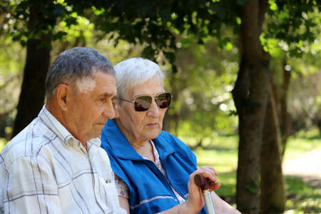 Elderly couple sitting on a bench with thoughtful faces expression. Rest in park, life in retirementの写真素材