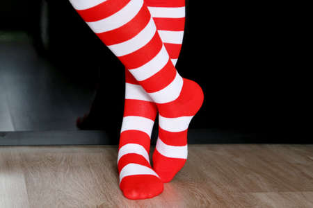 Female legs in Christmas knee socks on a floor on black wardrobe background. Clothing for New Year celebration, girl in Santa costumeの写真素材