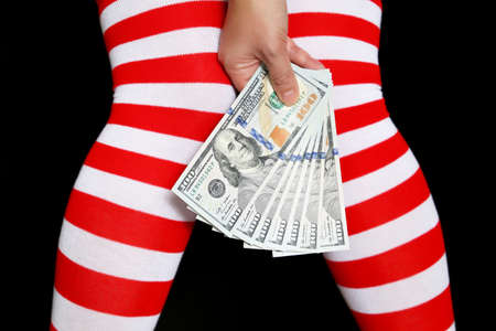 Woman in Christmas knee socks with dollars in hand. Female legs and US currency on black background, concept of New Year bonus, holiday shoppingの写真素材