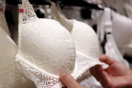Woman chooses white lace bra in lingerie store. Female fashion, different sizes of wedding underwearの写真素材
