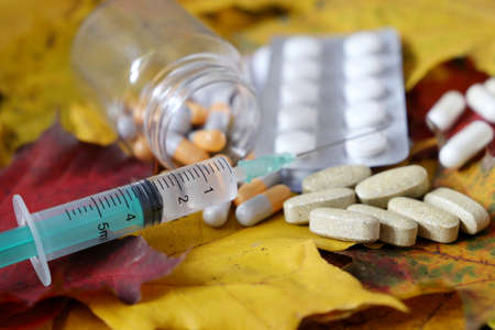 Syringe and pills on the autumn maple leaves. Health care during cold and flu seasonの写真素材