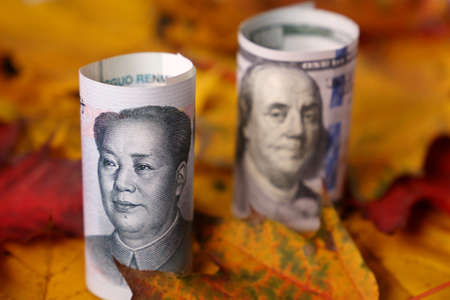 US dollar and chinese yuan banknotes on maple leaves. Concept of economy at autumn, trade war...