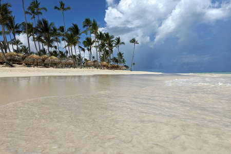 Tropical beach and ocean, view to white sand and coconut palm trees with wicker parasols. Sea resort, vacation on paradise islandの写真素材