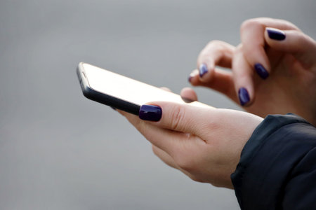 Female hands with smartphone close up on blurred background. Woman with manicure using mobile phone...