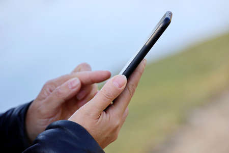 Female hands with smartphone close up on blurred background. Woman using mobile phone outdoors,...