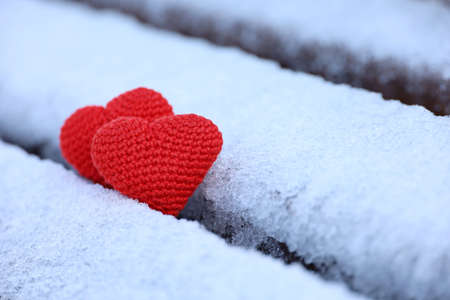 Knitted red hearts in the snow on a park bench. Valentine's card, two symbols of love, background for romantic event in winterの写真素材