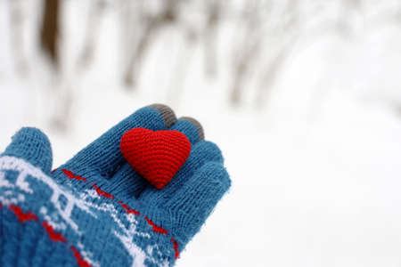 Red heart on palm of hand in warm knitted glove against the winter park and snow. Concept of a romantic love, Valentine's day or charityの写真素材