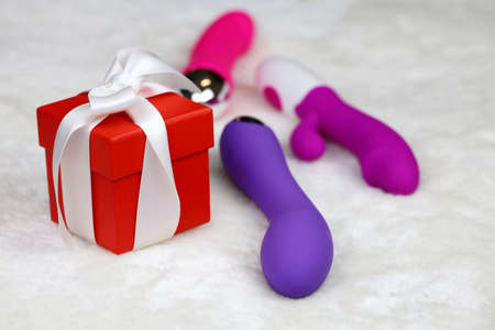 Red gift box and different sex toys on a bed. Purple silicone vibrators and red dildo for adult gamesの写真素材