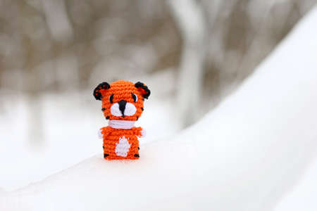 Knitted toy tiger on snow in a forest. Background for greeting card of celebration New Year 2022 of the tiger according to the Chinese calendarの写真素材