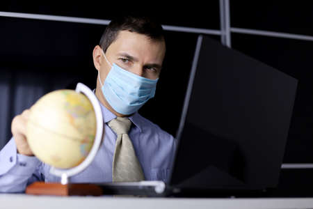 Man in mask looking the globe map sitting at laptop. Choosing travel tour, concept of tourism or...