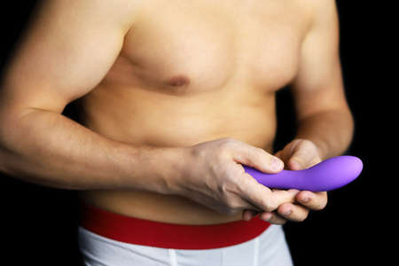 Dildo in male hands, sex toy. Muscular man in underpants with naked torso holding purple silicone vibrator, concept of adult games, stimulationの写真素材