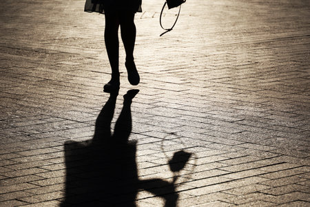 Black silhouette and shadow of lonely slim girl walking on a street. Female legs on sidewalk at autumnの写真素材