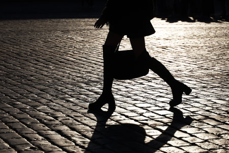 Black silhouette and shadow of slim girl walking on city street. Female legs in boots on high heelsの写真素材
