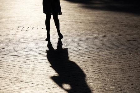 Black silhouette and shadow of lonely slim woman walking on a street. Female legs on sidewalk at autumnの写真素材