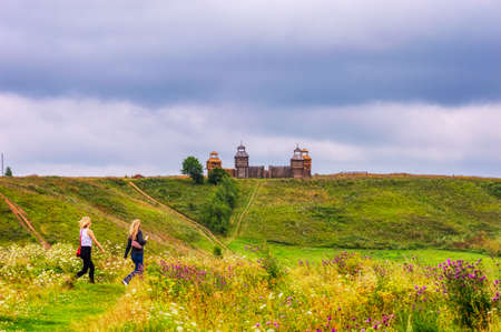 Two girls head to a wooden fortress on a hill on Pleshcheyevo lake, stormy weather dark clouds in the sky. Pereslavl-Zalessky, Russia, June 2018のeditorial素材