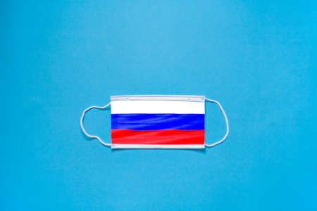 The concept of protection. Medical mask on the face, in the form of the flag of Russia on a blue...