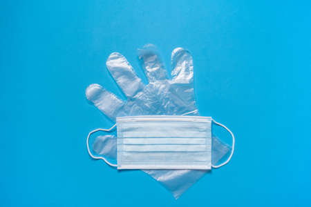 The concept of protection. Medical mask on the face and protective transparent gloves, on a blue background on top. A typical 3-layer surgical mask to cover the mouth and nose.の写真素材