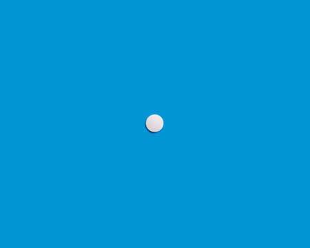 A single white tablet on a blue background. Medical pharmaceutical concept. The concept of lonelinessの写真素材
