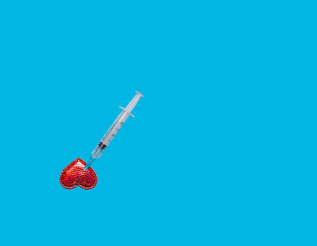 Top view of a red heart and an injection syringe on a blue background of a flat isolated image....