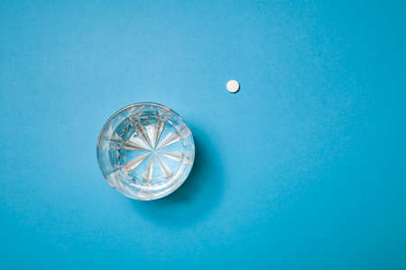 Tablets for the patient are on the table with water. A glass of water and white tablets on a blue background with harsh light and shadows. Creative. The concept of healthの写真素材