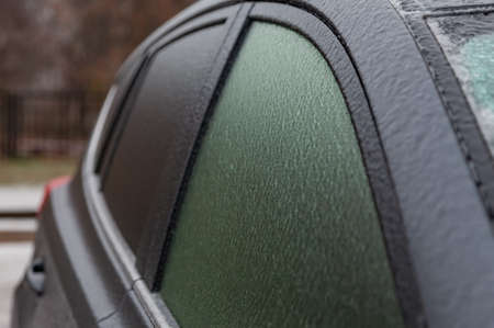 The side window and car mirrors of the black car are covered in icy rain. Car after an ice storm Bad weather for driving in freezing rain.の写真素材