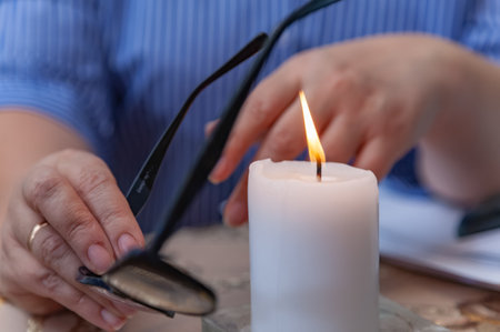 A lit white candle, women's hands holding glasses for vision. Magician, sorcerer, psychologist at workの写真素材