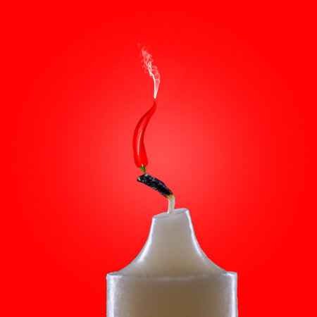 hot chili peppers on candles on a red background close-up with smoke. The candle burns with scalding red chiliの写真素材