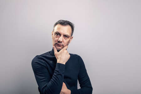 A white middle aged man of European appearance with gray in his hair and a slightly unshaven face in a black turtleneck clutches his head with both hands in despairの写真素材