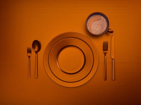 Orange cup of coffee and ceramic dishes with a set of cutlery fork, knife and spoon, top view. Empty red dishes for breakfast or dinner in a restaurant. Copyspace for your individual text.の写真素材