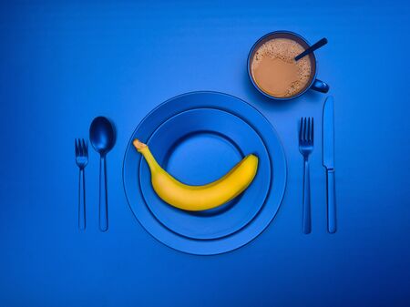 Blue dishes with banana on a plate. Cup of coffee with ceramic utensils with a fork, spoon and knife. For cafes, vegans, breakfasts and dinners. Copyspace for your individual textの写真素材