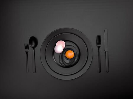 Black dishes with a broken egg and shell on a plate. Ceramic dishes with a fork, spoon and knife. For cafes, posters, breakfasts and dinners. Copyspace for your individual textの写真素材