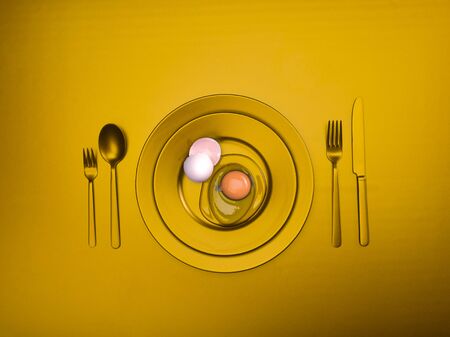 Gold plate with a broken egg and shell on a plate. Ceramic dishes with a fork, spoon and knife. For cafes, posters, breakfasts and dinners. Copyspace for your individual textの写真素材
