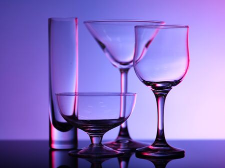 Empty beautiful glasses stand on the glass and shot on a multi-colored background in purple hueの写真素材