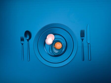 Blue dishes with a broken egg and shell on a plate. Ceramic dishes with a fork, spoon and knife. For cafes, posters, breakfasts and dinners. Copyspace for your individual textの写真素材