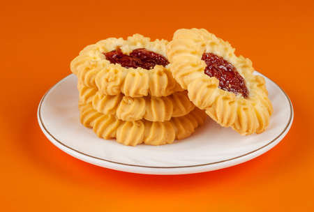 Four butter cookies, strawberry jam tartlets in a white saucer
