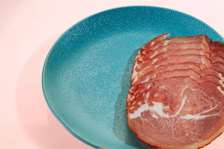 Delicious and appetizing smoked meat cut into thin slices on a blue plateの写真素材