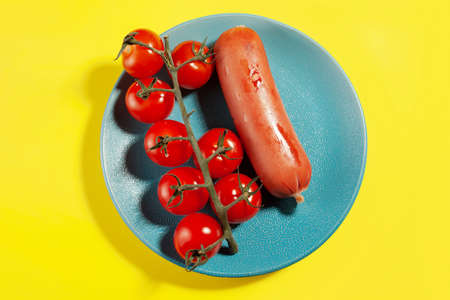 Fried delicious sausage and delicious cherry tomatoes on a plate on a yellow backgroundの写真素材