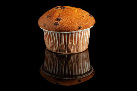 Muffin with chocolate drops, in a paper wrapper, on a glossy black backgroundの写真素材