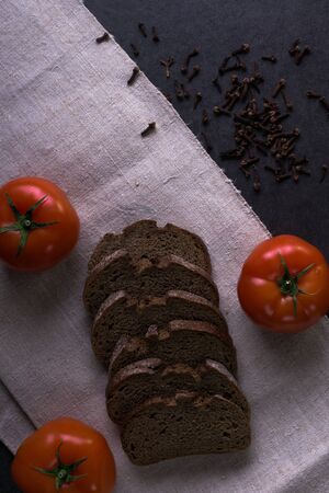 Background food ingredients on the tablecloth. Fresh tomatoes, homemade bread and cloves.の写真素材